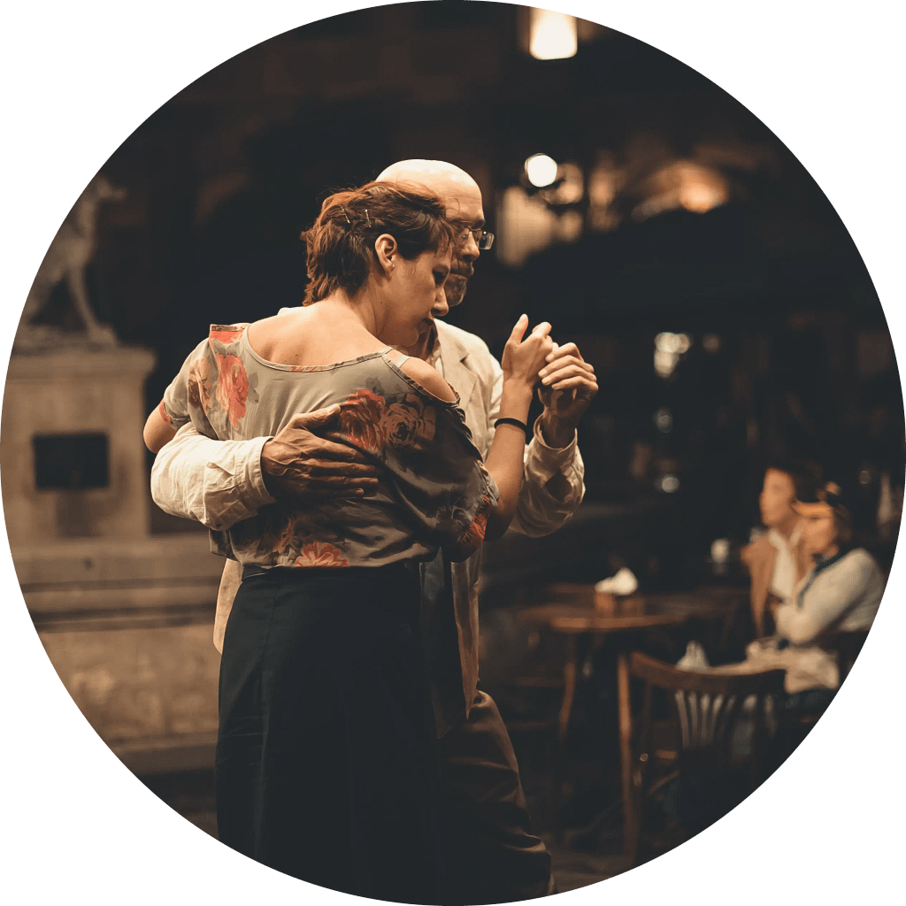 Imagen circular que muestra a una pareja bailando tango sobre la vereda frente a un conocido café de la ciudad de Buenos Aires, Argentina