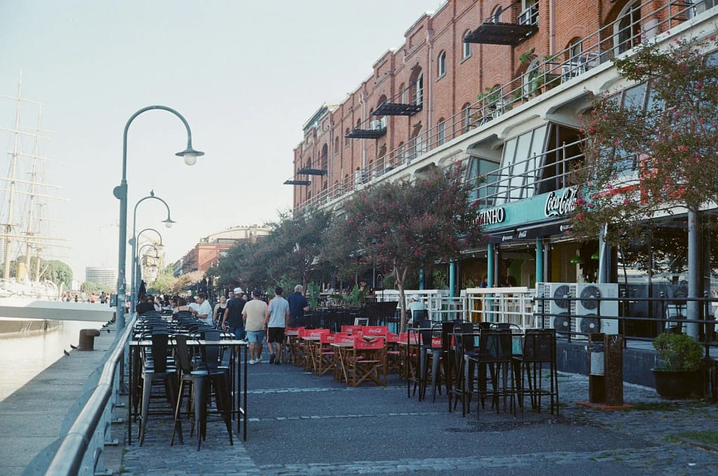 Turistas caminan frente a restaurantes premium con vista al río en Puerto Madero, Buenos Aires.