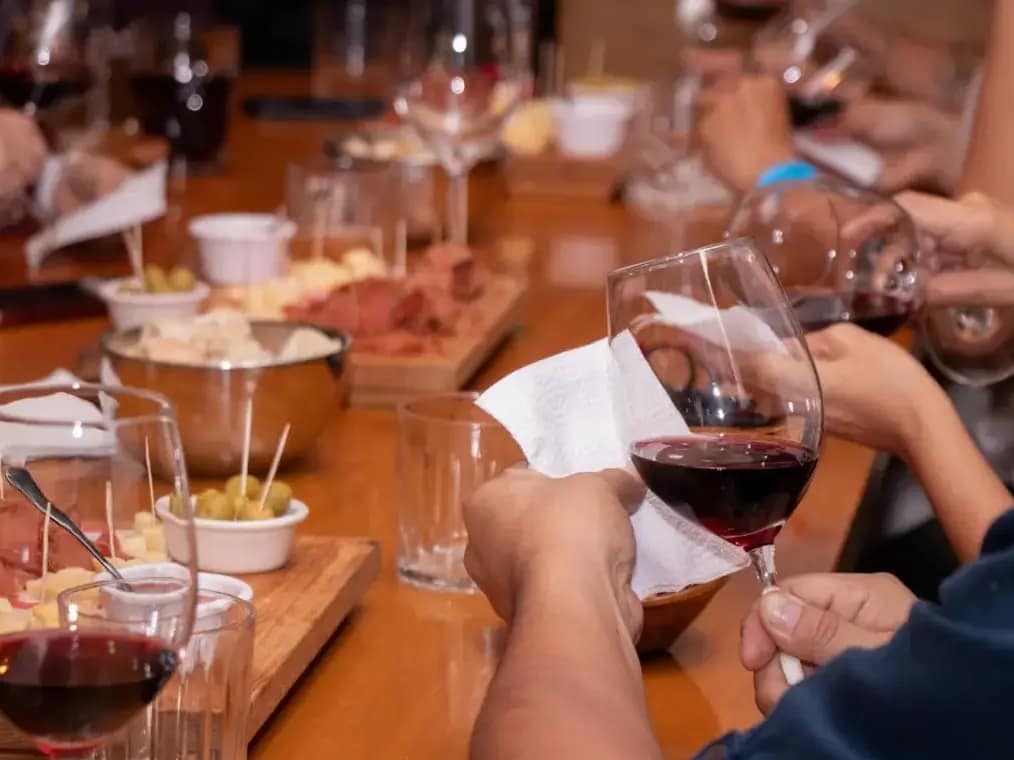 Cata de vino en bodegas de Mendoza, Argentina. Primer plano de manos de personas sosteniendo copas de vino en un evento de cata de vinos con bocadillos en una mesa de madera.