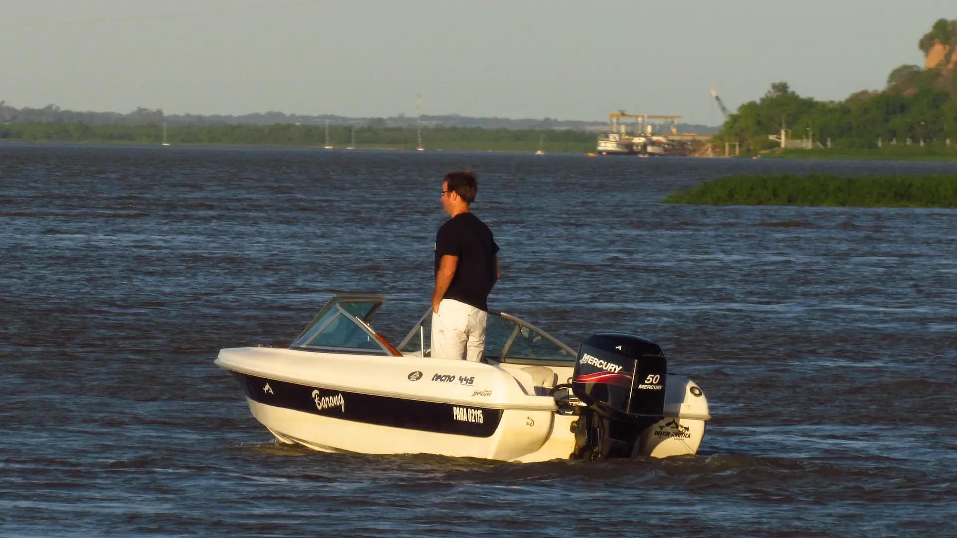 Joven disfrutando de un paseo náutico en lancha con motor fuera de borda en el río Paraná, con la ciudad de Paraná de fondo